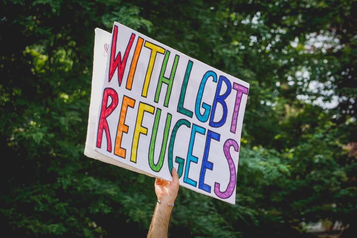 A person holds a sign that says "With LGBT Refugees"